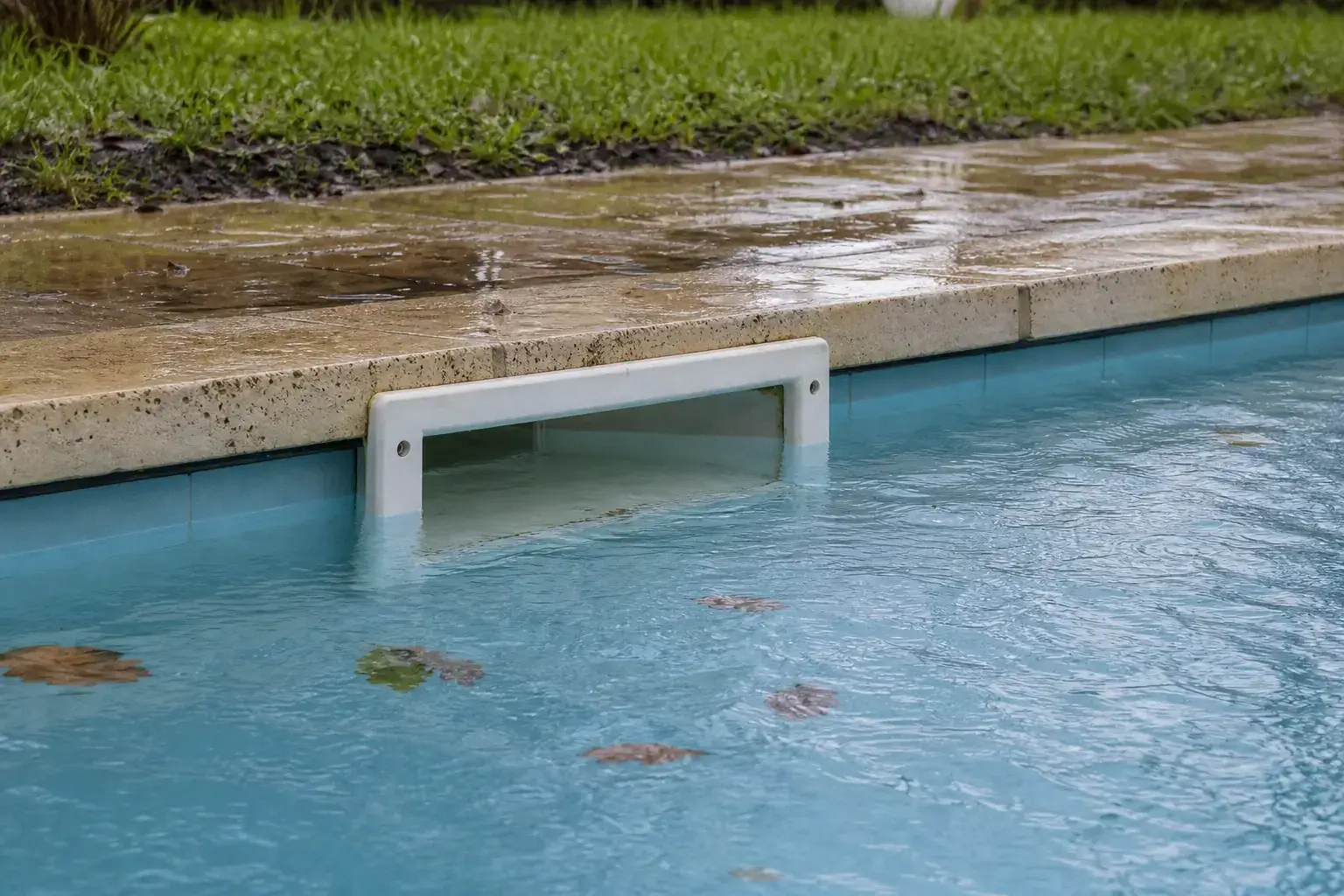 Eau de piscine montée presque en haut du skimmer après la pluie, devant une terrasse et un sol détrempés